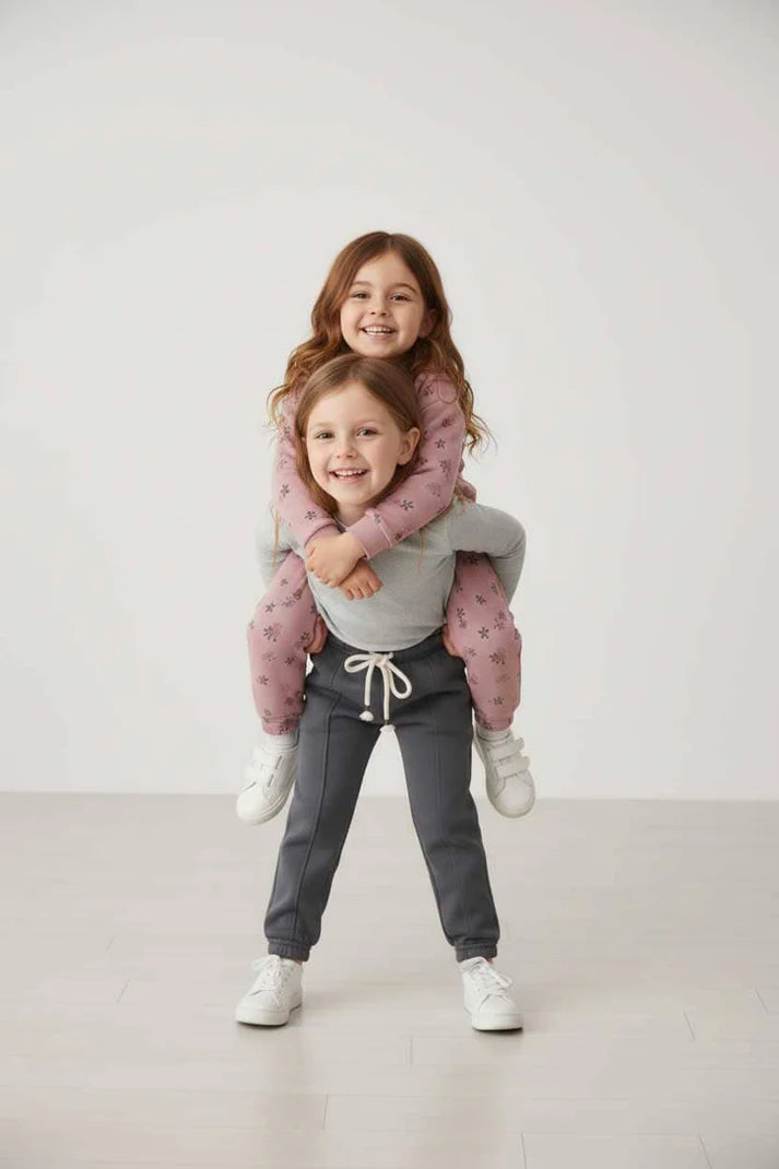 Two children standing on a plain background, one child piggybacking the other.