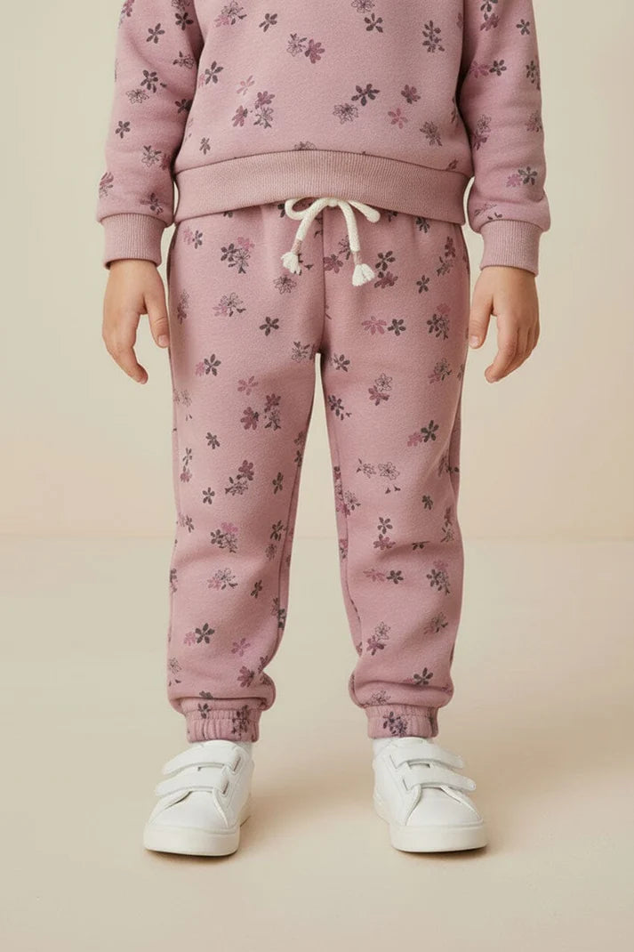 Child wearing a pink floral tracksuit with white sneakers on a beige background