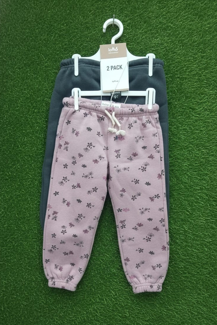 Two pairs of children's pants on a hanger against a green background